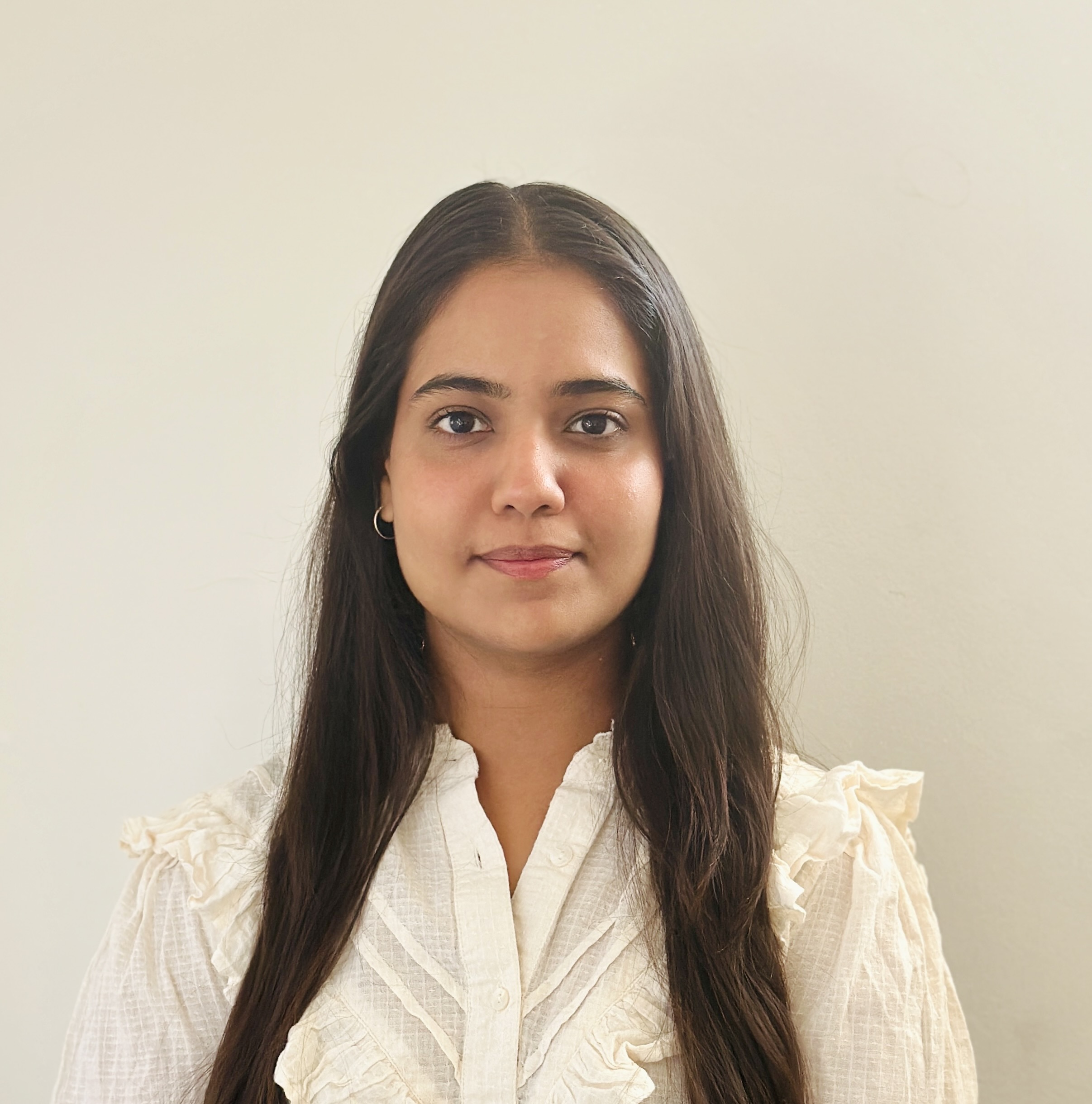 Portrait of Sakshi Kaushal, a young woman with long brown hair, wearing a white ruffled blouse, smiling subtly at the camera against a plain background.