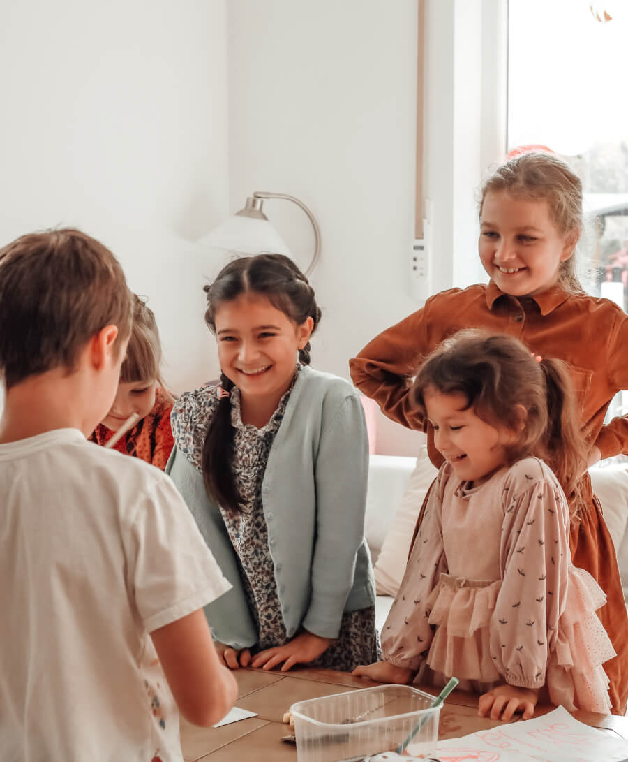 Group of children gathered around a table, smiling and engaged in an indoor activity.