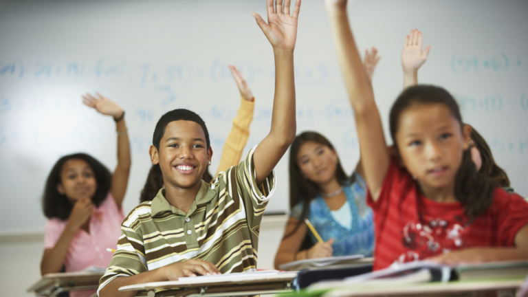 Children raising their hands in a classroom.