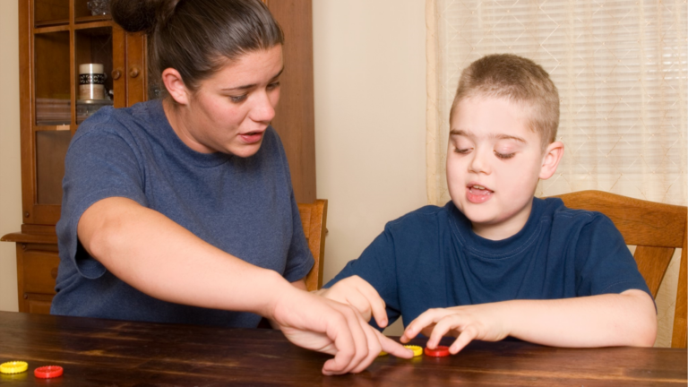 A woman helping a boy with autism play a game.