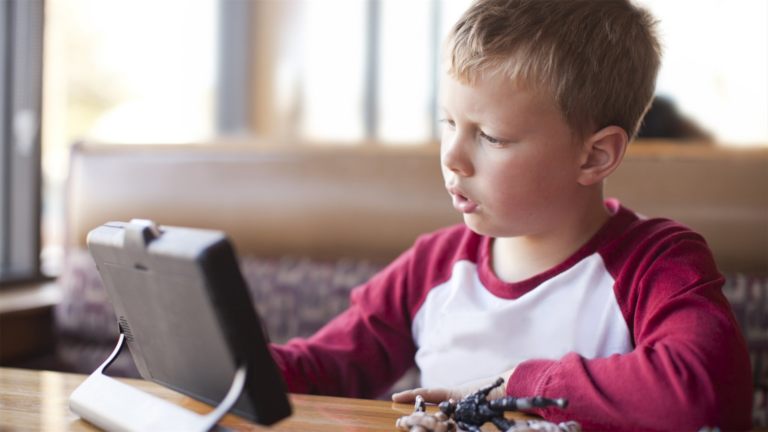 A young boy sitting at a table with a tablet computer.