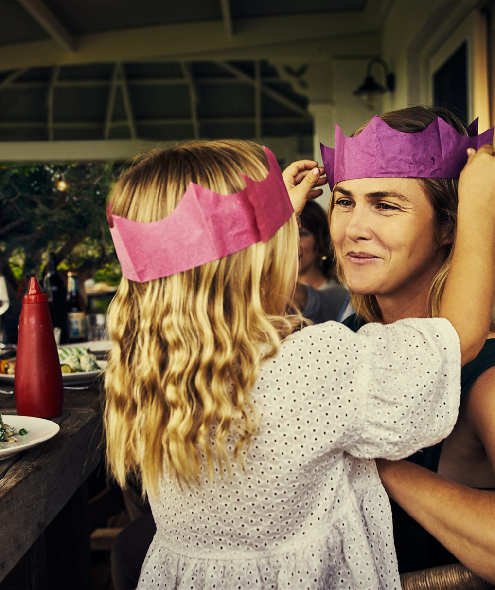 A mother and daughter wearing crowns at a party.